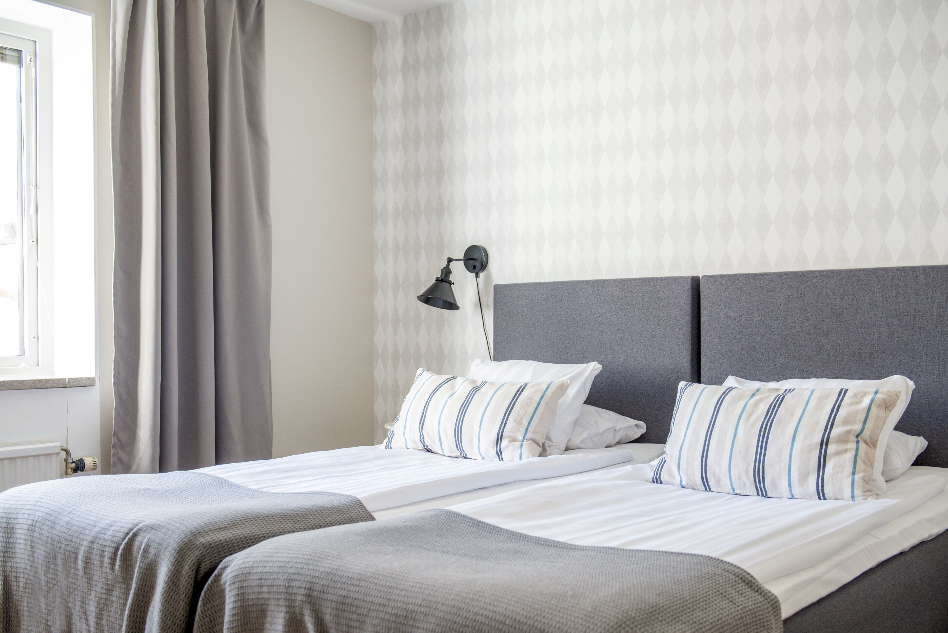 A hotel room with a bed, a nightstand, a lamp, and a window with curtains.