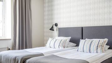 A hotel room with a bed, a nightstand, a lamp, and a window with curtains.