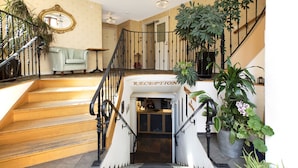 A grand staircase leading to a reception area with a sign, surrounded by potted plants and a chandelier. - Hotell Lindgården (Visby)