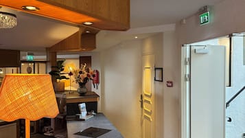 A hotel lobby with a reception desk, a lamp, a vase with flowers, and a staircase.