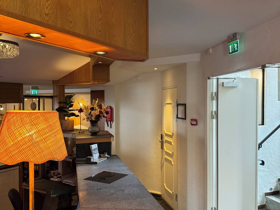 A hotel lobby with a reception desk, a lamp, a vase with flowers, and a staircase.