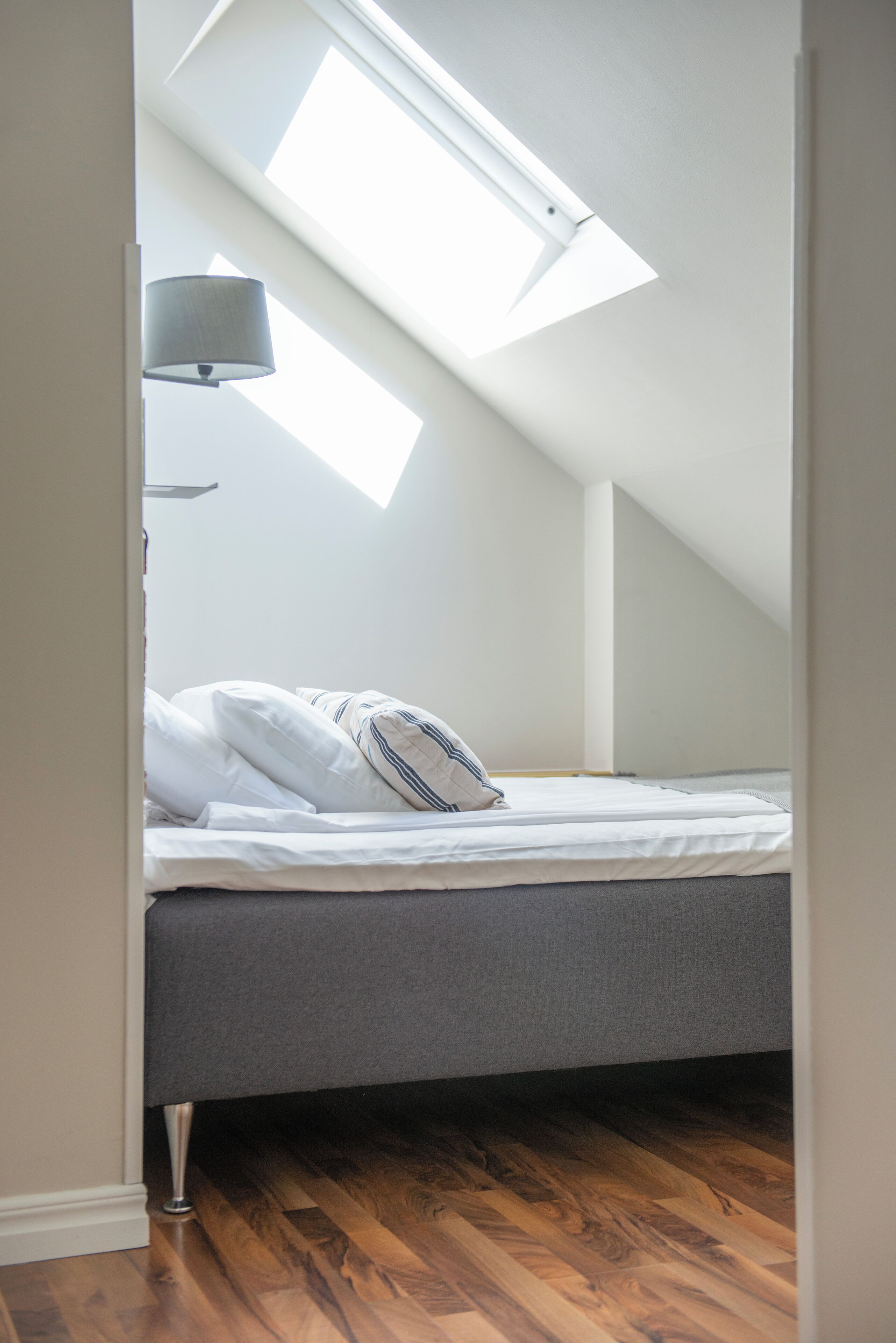 Una camera da letto con un lucernario, un letto con biancheria grigia e una lampada da comodino.