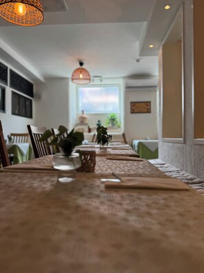 A dining area with a long table set for a meal, chairs, a vase with flowers, and a hanging light fixture. - Hotell Lindgården (Visby)