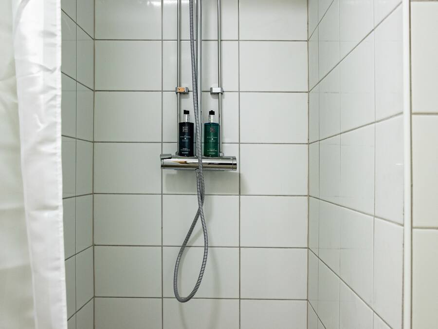 A small, tiled shower stall with a showerhead and a handheld shower attachment.