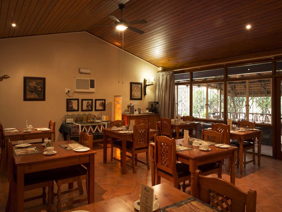 A dining area with wooden tables and chairs, a ceiling fan, and a view through large windows.