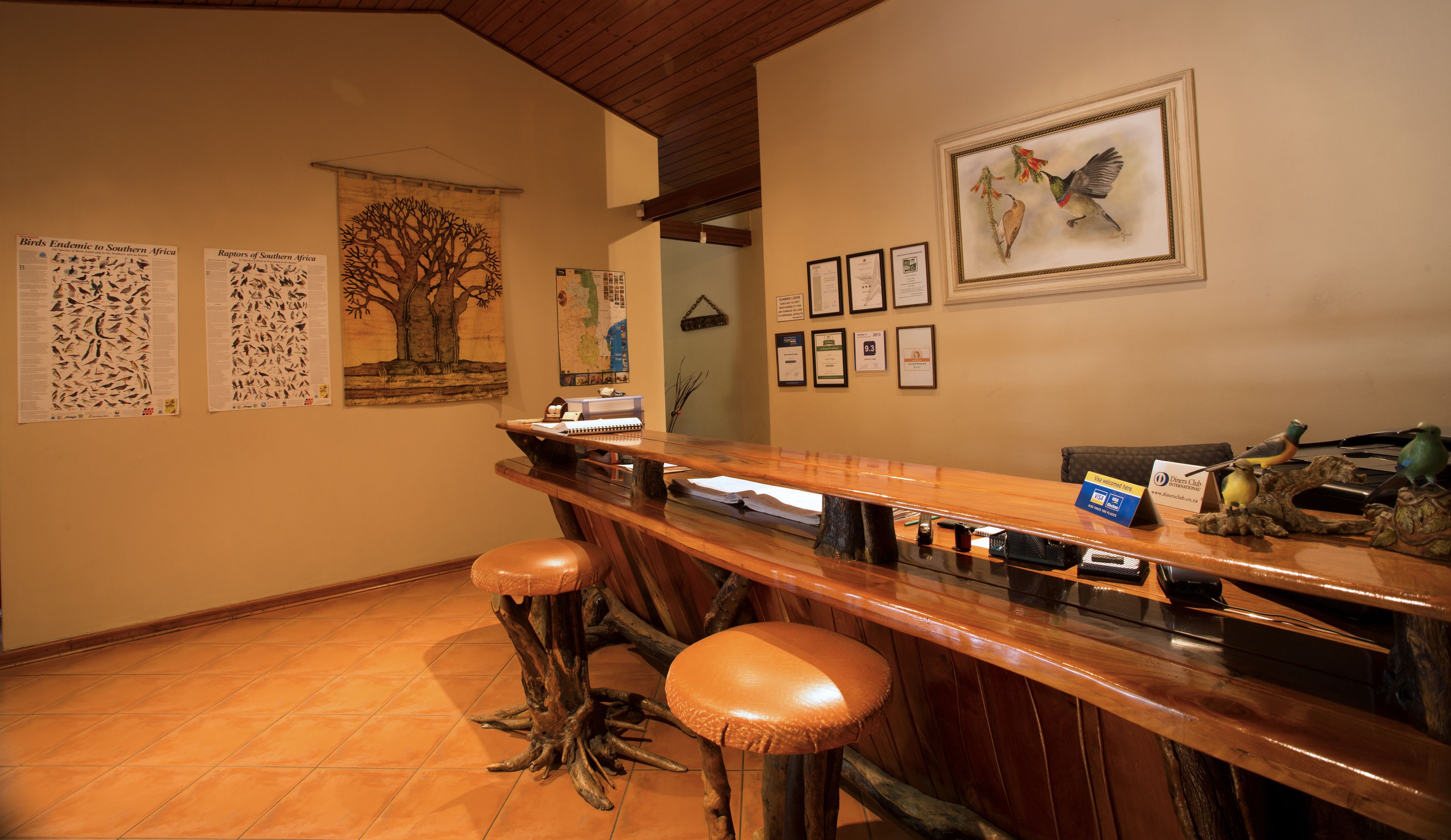 Un espace bar avec un comptoir et des tabourets en bois, des illustrations d’oiseaux encadrées au mur et une carte.