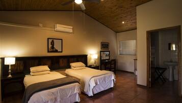 A hotel room with two beds, a ceiling fan, a wooden ceiling, and a bathroom visible through an open door.