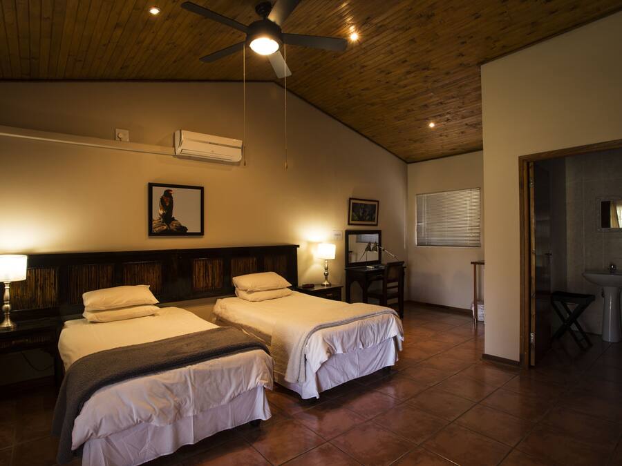 A hotel room with two beds, a ceiling fan, a wooden ceiling, and a bathroom visible through an open door.