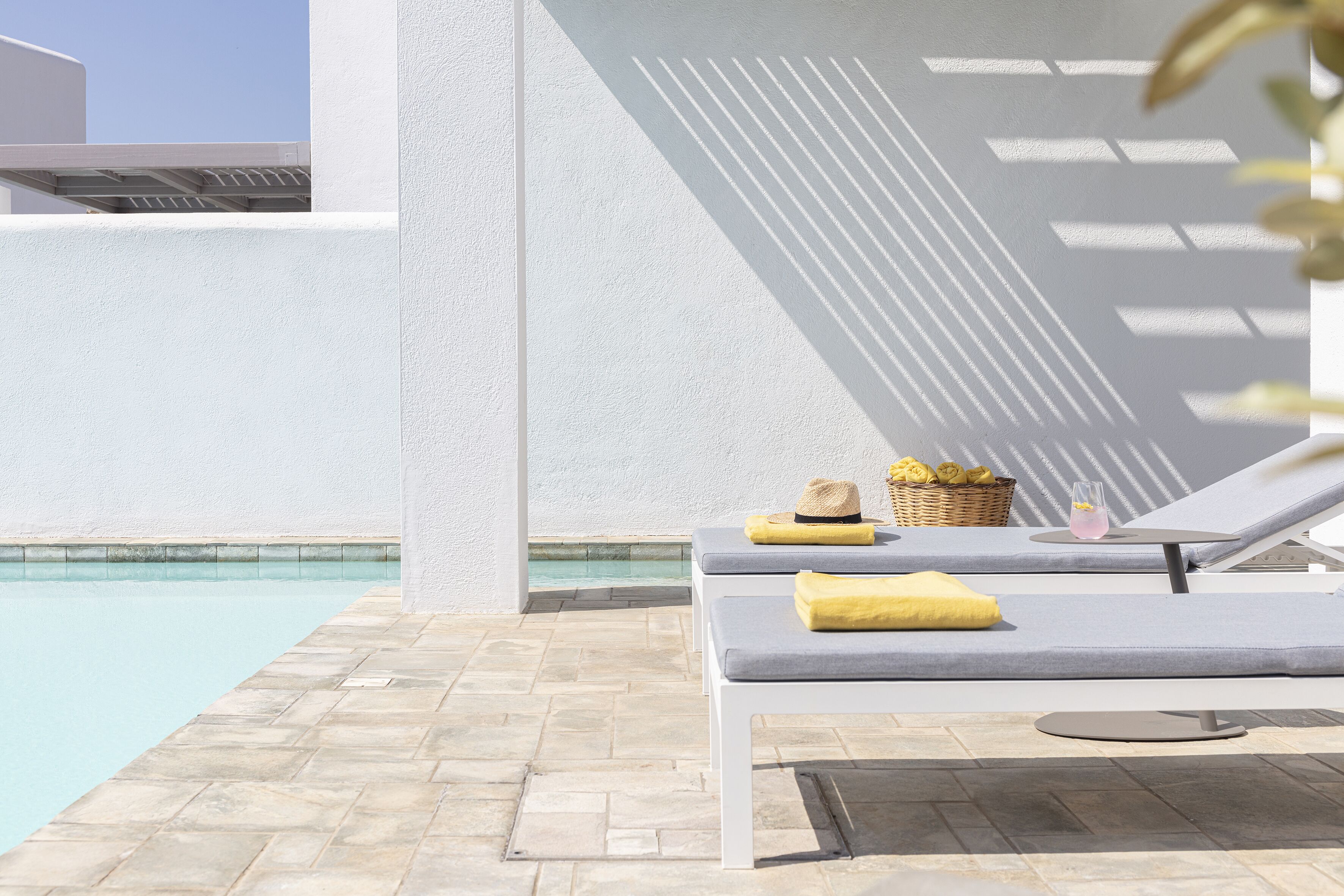A poolside area with two lounge chairs, a small table with a drink and a basket of lemons, and a clear view of the pool.