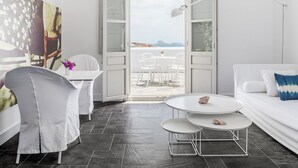 A modern, minimalist room with a large window, white furniture, and a view of the sea.