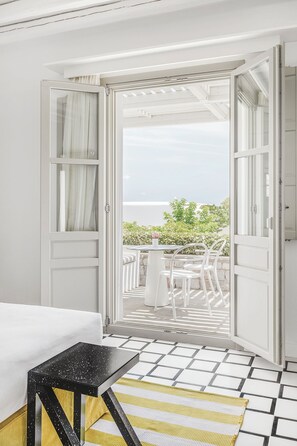 Una habitación con cama, una mesita y una puerta abierta que da a un espacio al aire libre con vistas a la vegetación y el cielo.
