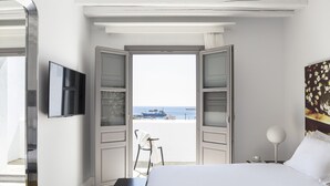 A hotel room with a bed, a TV, a painting, and a view of the sea.