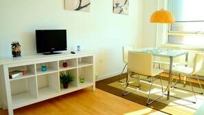 A room with a white TV stand, a desk with a chair, a lamp, and artwork on the wall. - Studio Rådmandsgade (Copenhagen)
