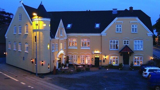 A traditional European-style building with a central entrance, multiple windows, and a well-lit facade. - Højslev Kro (Hojslev)