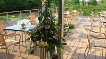 An outdoor patio area with tables and chairs, surrounded by greenery.
