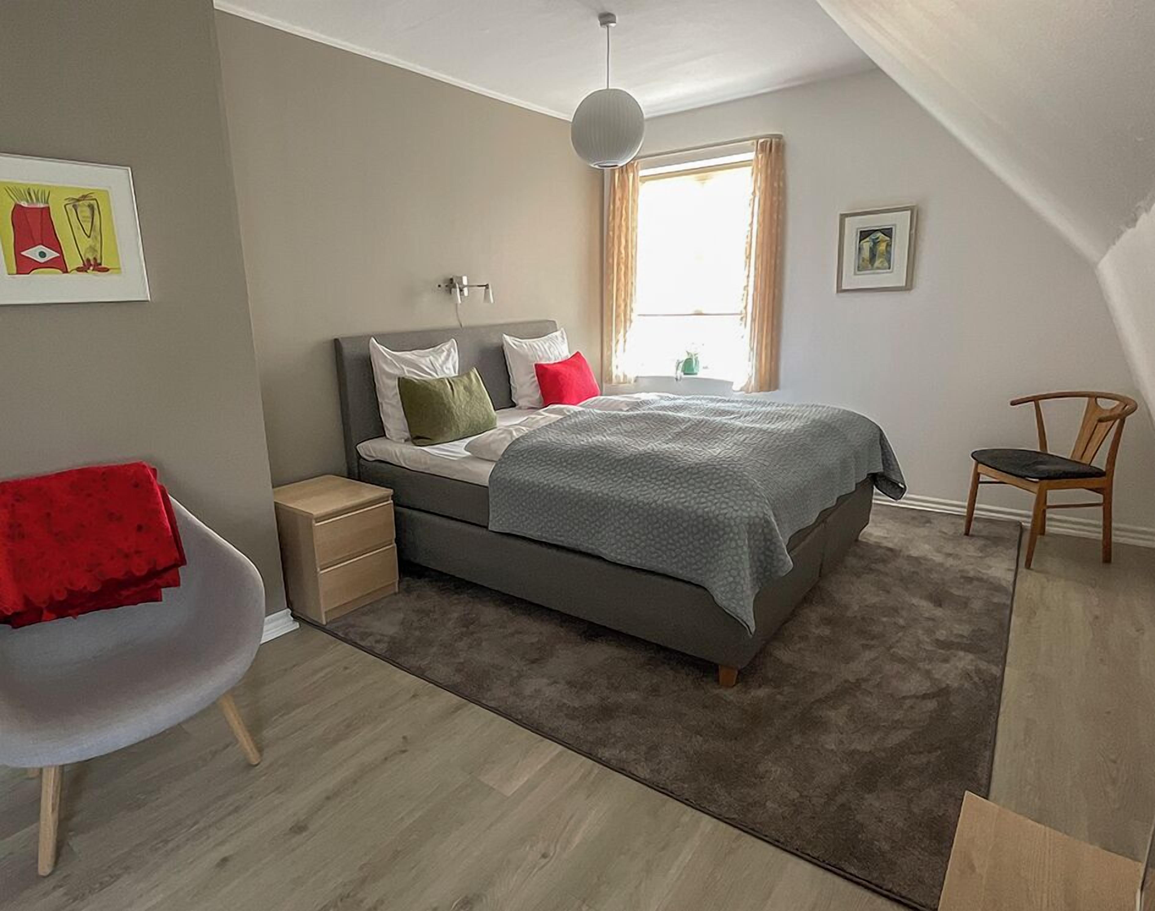 A modern bedroom with a bed, bedside tables, a chair, and a window.