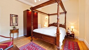 A four-poster bed with a wooden frame, a red and white patterned rug, a wooden chair, and a small table with a lamp. - Højslev Kro (Hojslev)