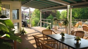 An outdoor patio with wicker furniture, potted plants, and a view of greenery. - Højslev Kro (Hojslev)
