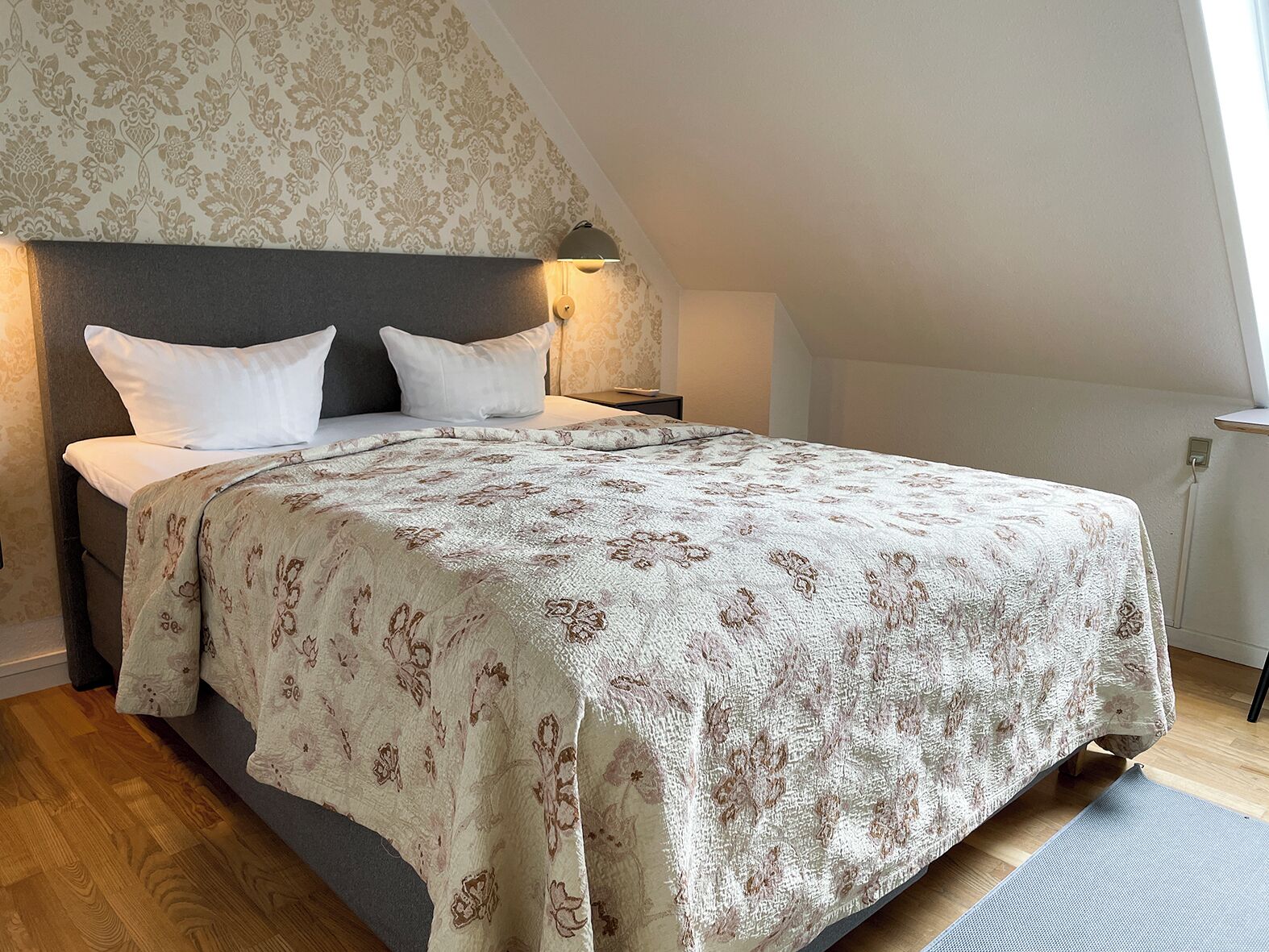 A bedroom with a large bed, a headboard, a nightstand, and a wall-mounted lamp.