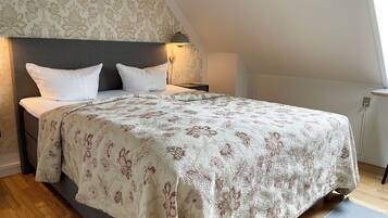 A bedroom with a large bed, a headboard, a nightstand, and a wall-mounted lamp.