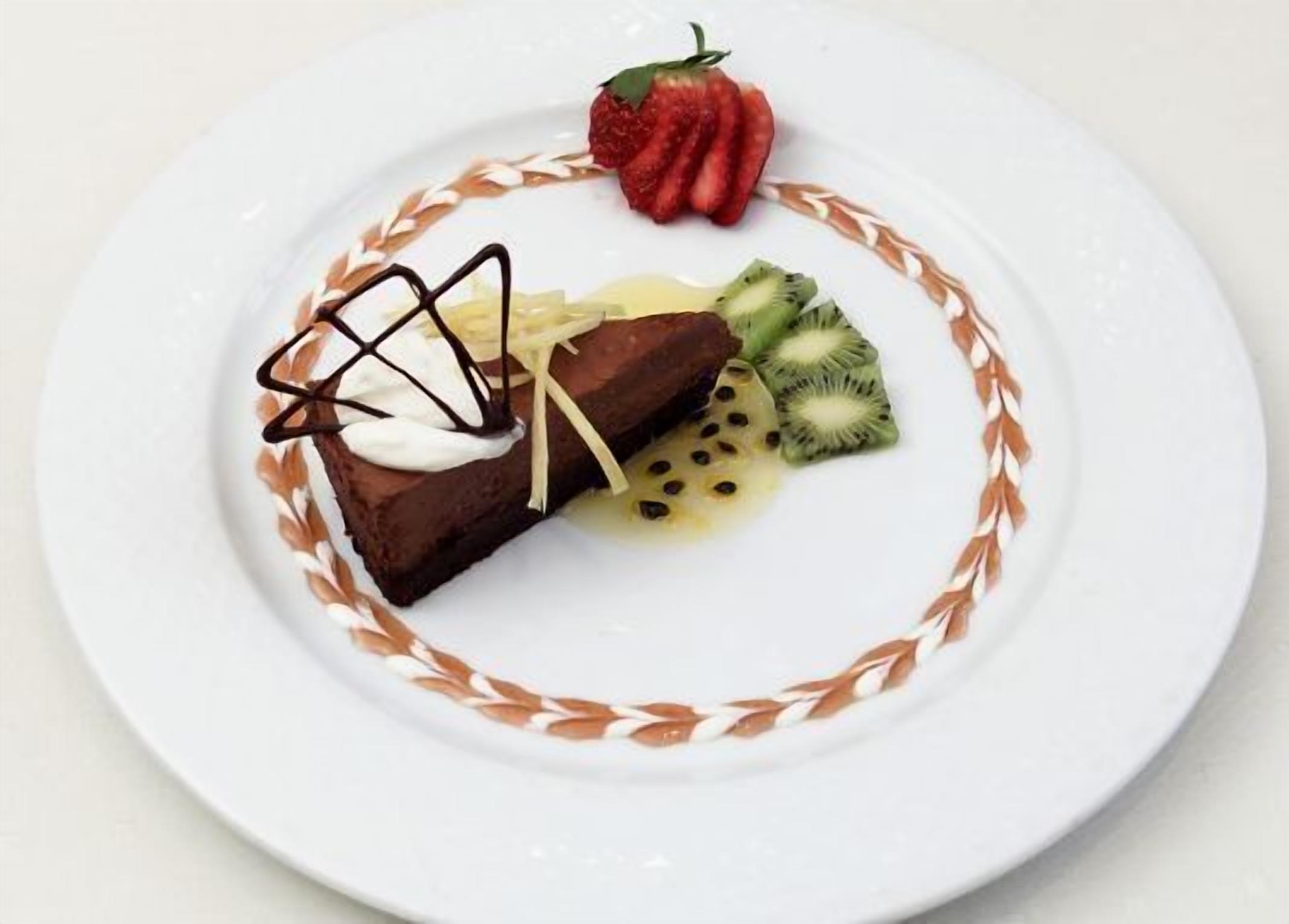 A dessert with chocolate, whipped cream, and fruit on a white plate with a decorative border.