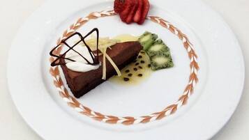 A dessert with chocolate, whipped cream, and fruit on a white plate with a decorative border.
