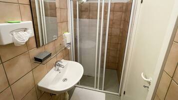 A bathroom with a shower enclosure, a sink, a toilet, and a mirror.