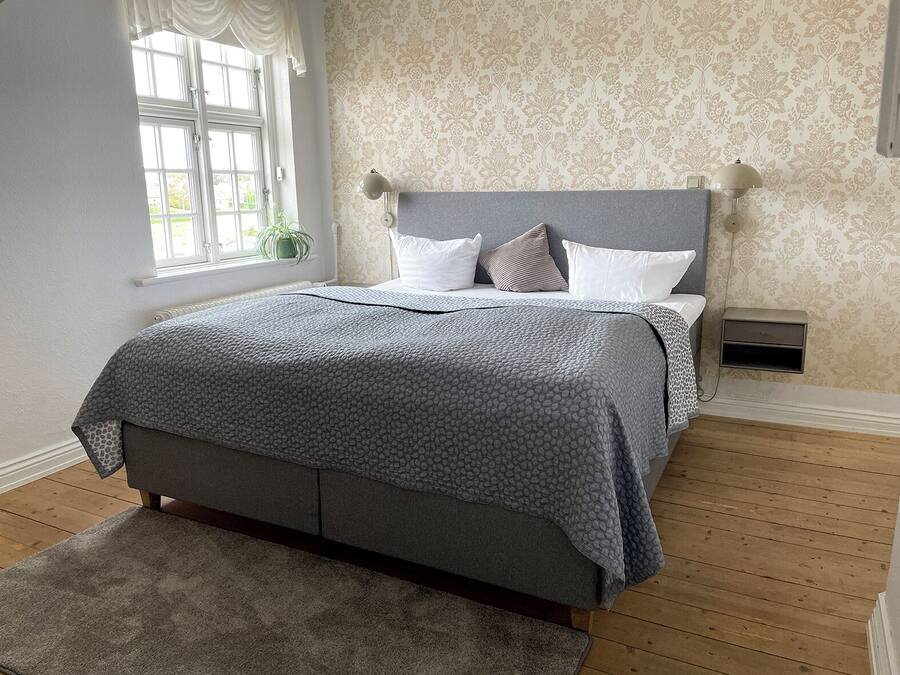 A bedroom with a bed, a nightstand, a lamp, and a window with curtains.