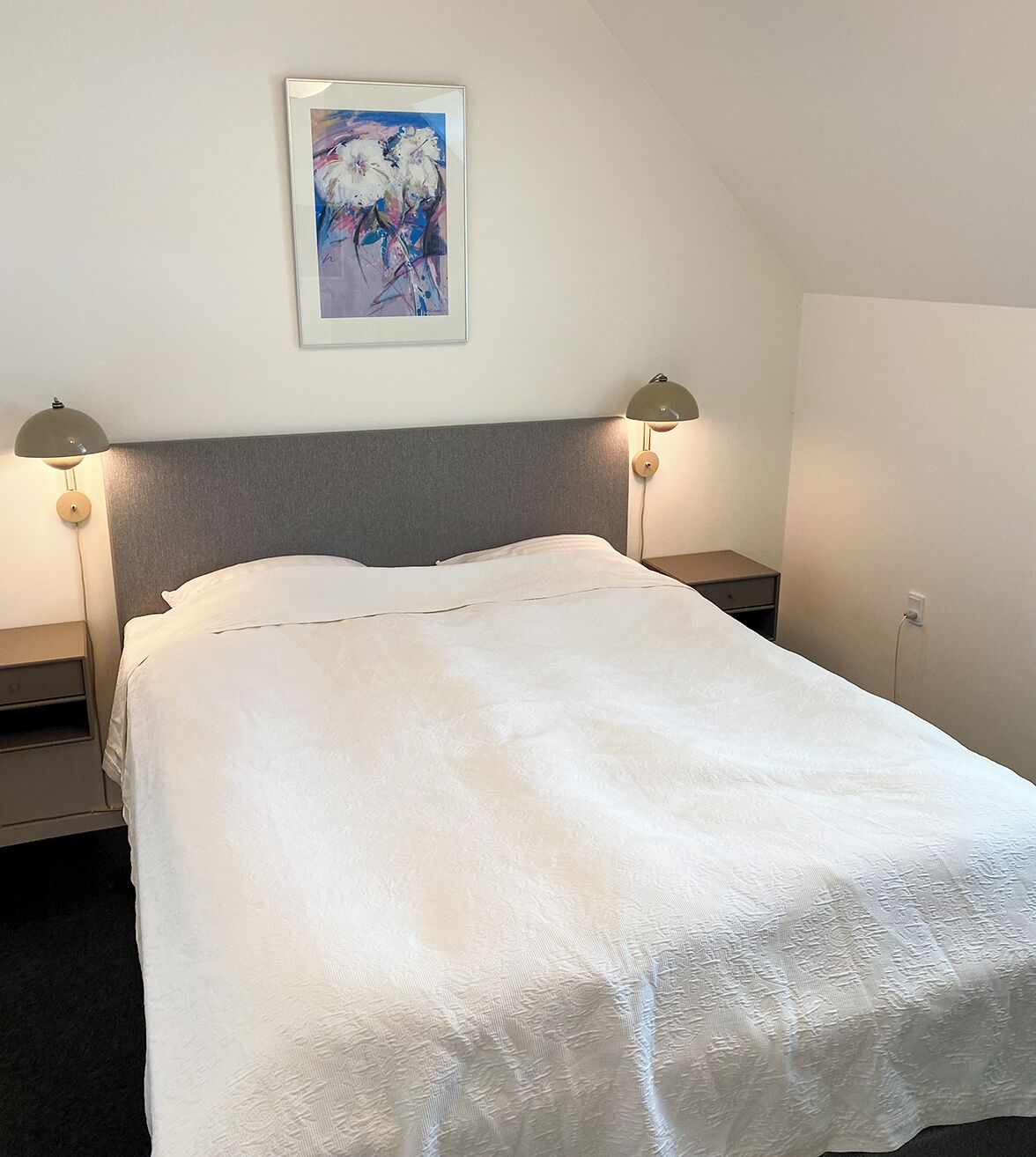 Un lit bien fait, avec une couette blanche et deux lampes de chevet.