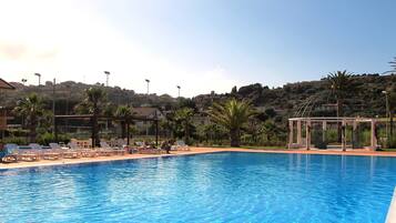 Relax by the serene pool surrounded by lush greenery and Mediterranean-style buildings.