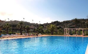 Una piscina al aire libre, sombrillas, sillones reclinables de piscina