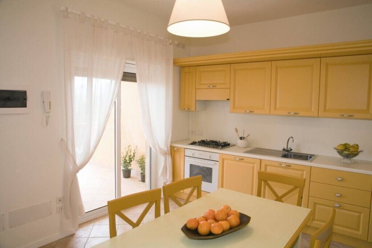 A kitchen with yellow cabinets, a stove, and a sink. There is a table with chairs and a bowl of oranges.