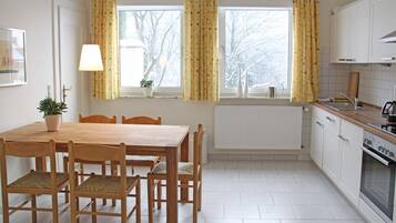 Eine Küche mit Esstisch, Stühlen, Heizkörper, Fenster mit Vorhängen und Spüle.