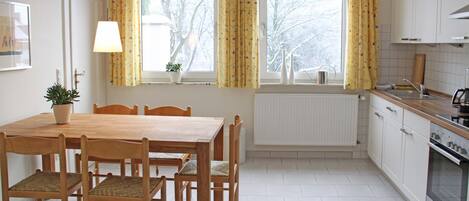 A kitchen with a dining table, chairs, a radiator, a window with curtains, and a sink.