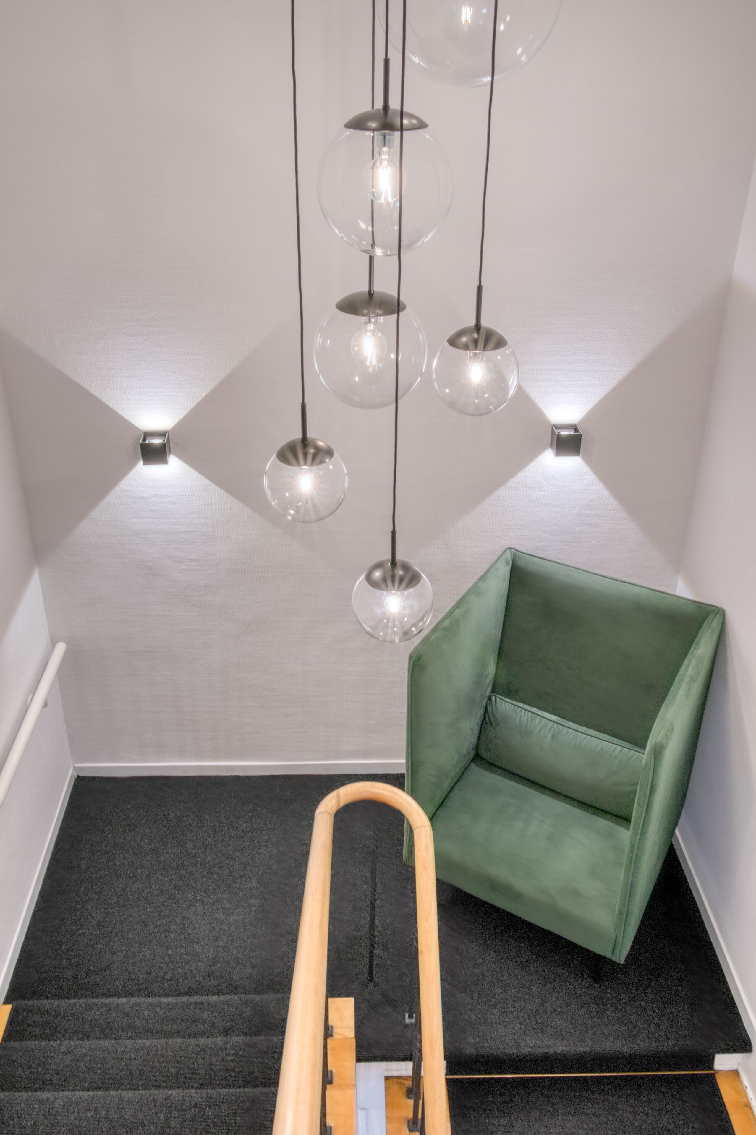 A staircase with a green chair, a wooden handrail, and multiple hanging spherical light fixtures.