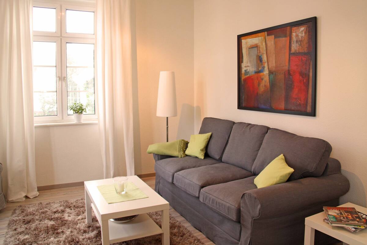A living room with a grey sofa, a white coffee table, a lamp, and a painting on the wall.