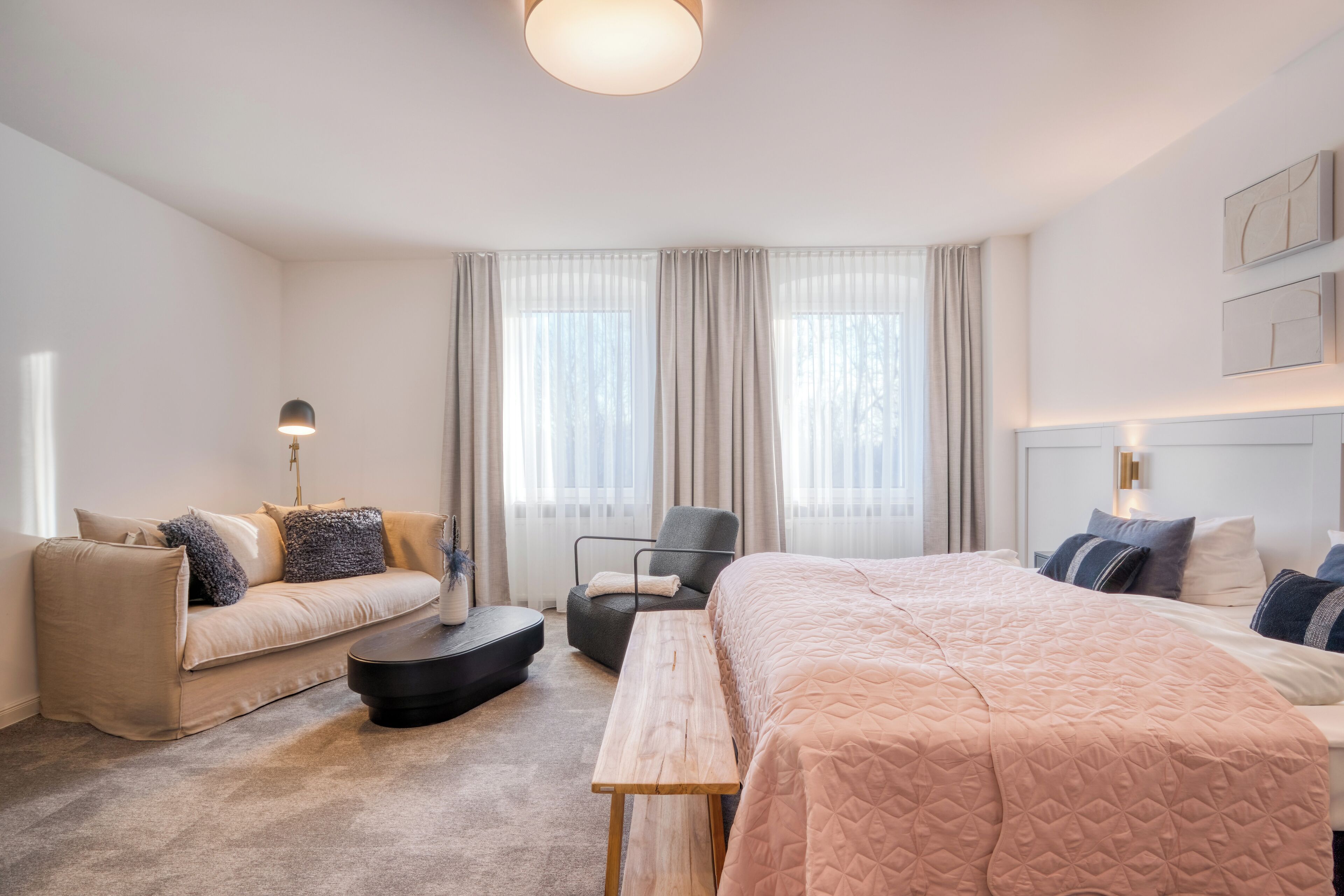 Una habitación de hotel con una cama, un sofá, una silla, una mesita y una lámpara.
