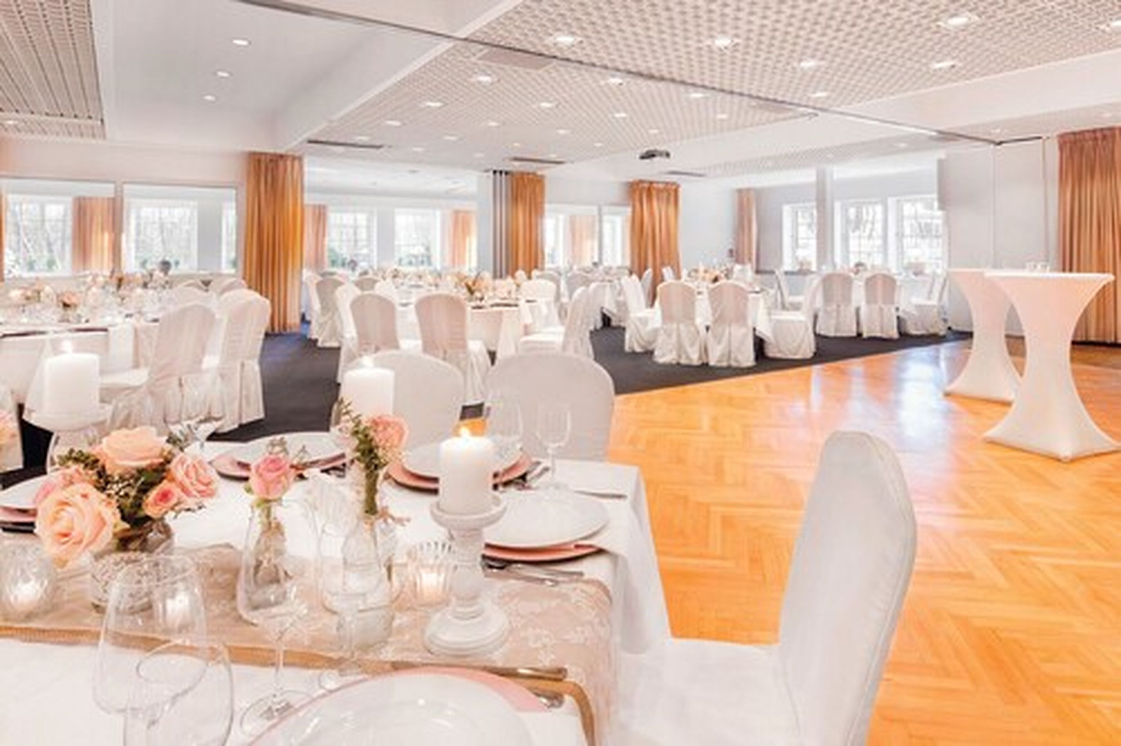 A large banquet hall with round tables set for a formal event, featuring white tablecloths, floral centerpieces, and white chairs.