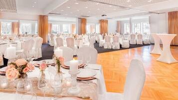 A large banquet hall with round tables set for a formal event, featuring white tablecloths, floral centerpieces, and white chairs.