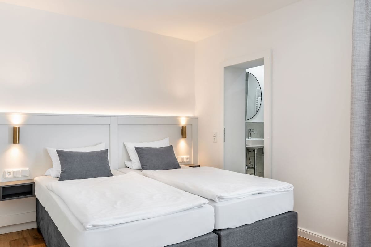 A double bed with two bedside tables, a mirror, and a bathroom with a sink and mirror.