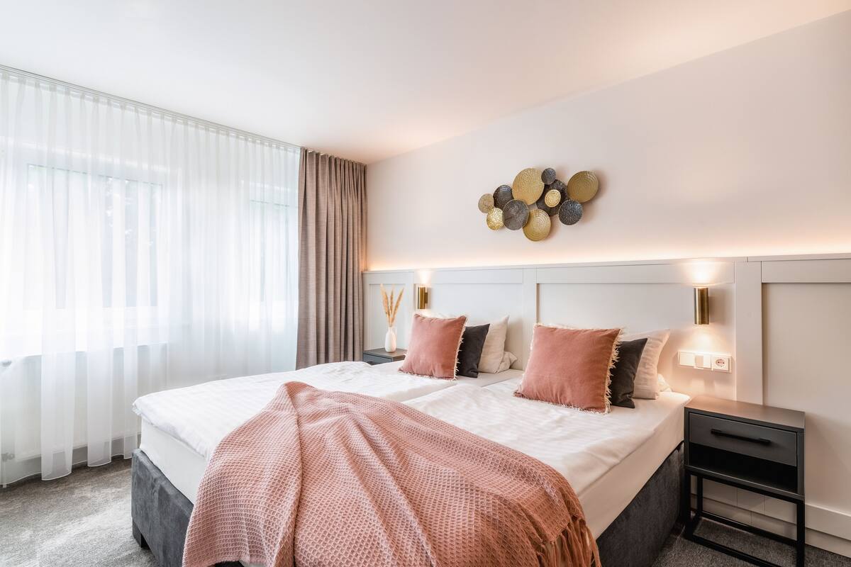 A modern bedroom with a large bed, bedside tables, and a decorative wall piece.