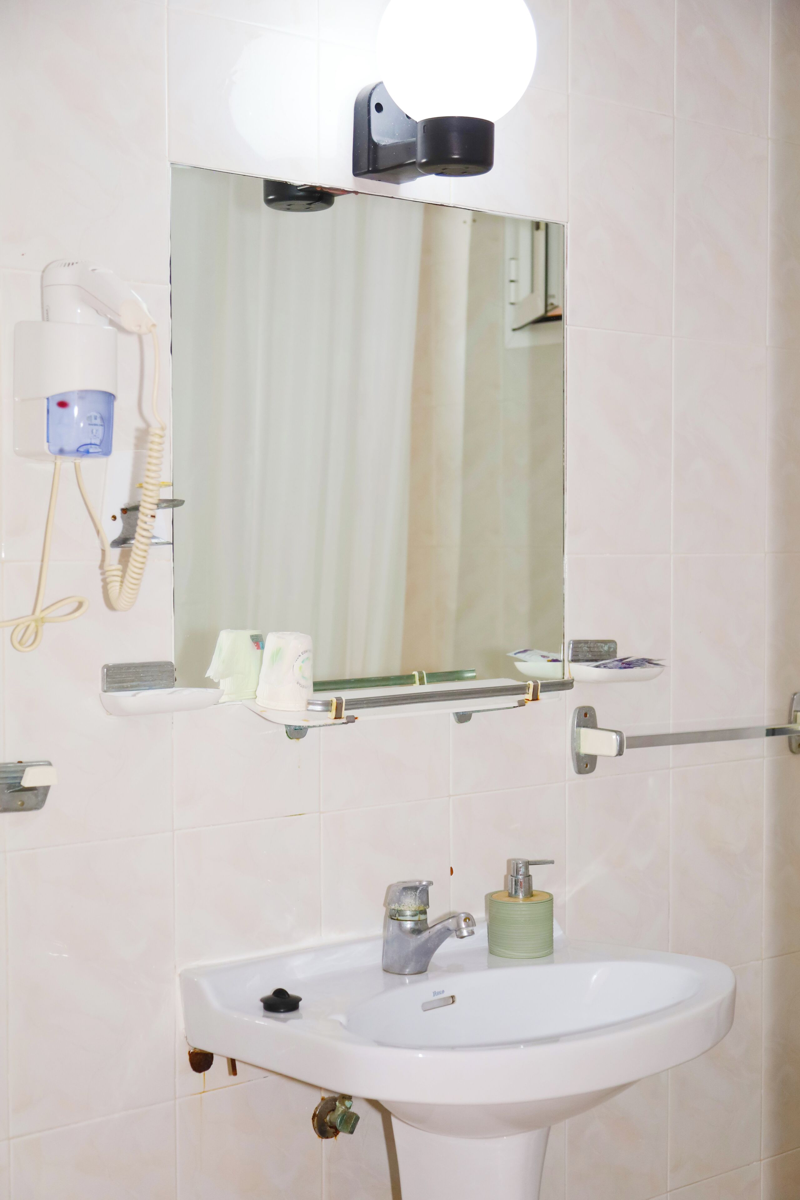 Baño con lavamanos, espejo y secador de pelo sujeto a la pared.