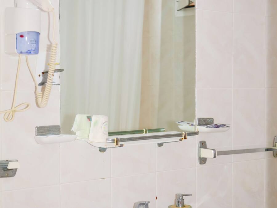 Baño con lavamanos, espejo y secador de pelo sujeto a la pared.