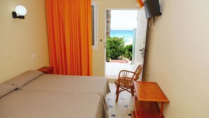 A room with two beds, a wooden chair, a small table, and a view of the beach.