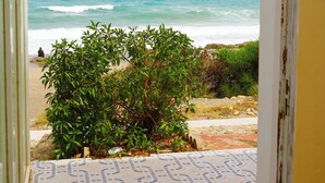 A view from a room with patterned floor tiles to a beach with waves and a person in the distance.