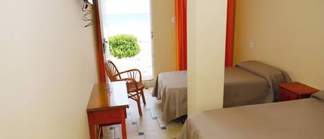 Habitación de hotel con dos camas, un escritorio y una silla. Se ve la playa a través de una puerta abierta.