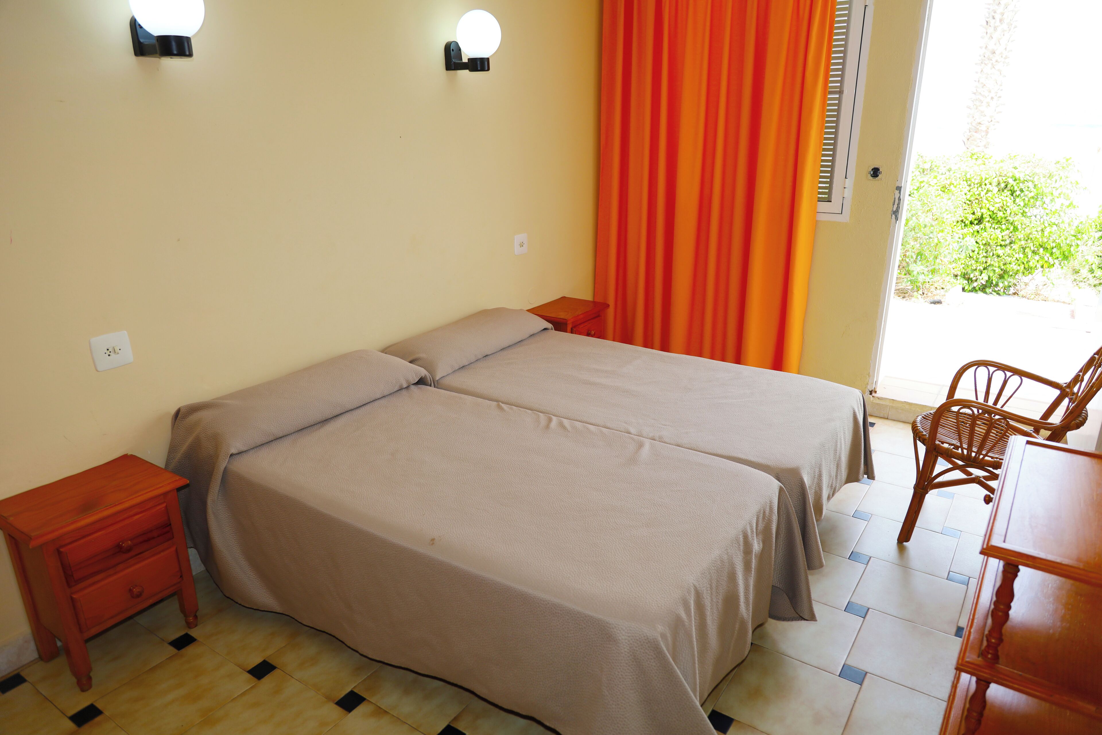 A room with two beds, a wooden nightstand, a chair, and a table.