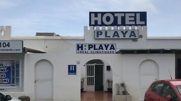 Un hotel llamado "HOTEL PLAYA" con un letrero que indica "CLIMATIZADO LOCALMENTE" y una señal azul con el número "30".