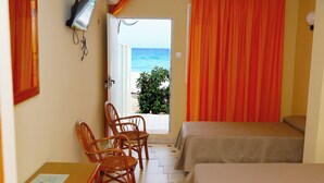 A room with two beds, a table, and chairs. There is a view of the beach through an open door.