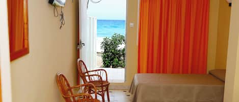Una habitación con dos camas, una mesa y sillas. Se ve la playa desde una puerta abierta.